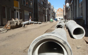 Een opengebroken straat in de binnenstad met grote buizen die klaar liggen.