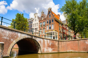 Een gracht met een brug, woningen en bomen.