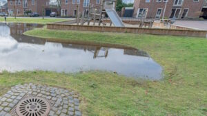 Speeltuin en grasveld in een woonwijk met een grote plas water.