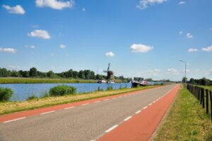 Een weg langs een watergang met op de achtergrond boten en een molen.