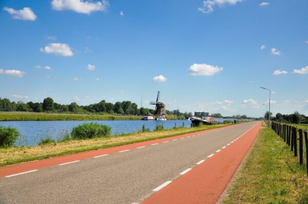 Een weg langs een watergang met op de achtergrond boten en een molen.