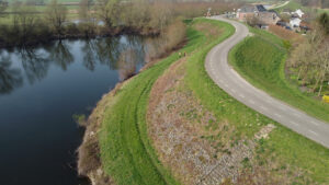 Een luchtfoto van een dijk met een weg en op de achtergrond een woning. Meerdere personen lopen op de dijk.