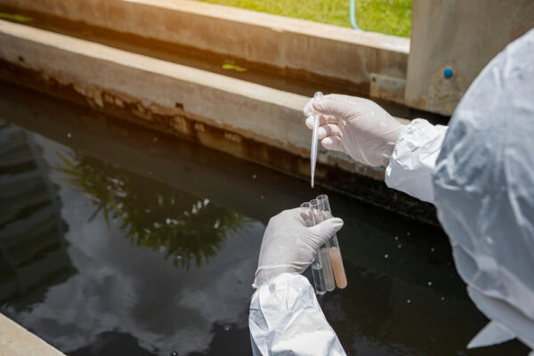 Een persoon in beschermende kleding neemt in een pipet monsters uit water.