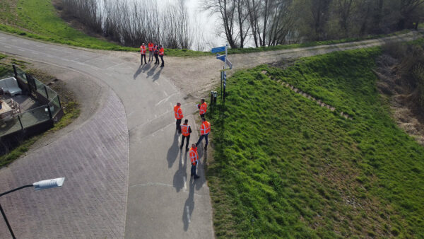 Personen in oranje jassen op een dijk.